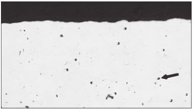 Figure 3.6 Pitting (arrow) on the surface of a cold-drawn brass (Cu-20% Zn) specimen (100X).