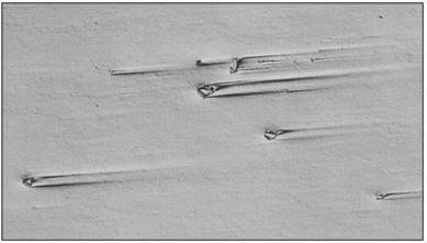 Figure 3.7 Comet tails at large nitrides in an annealed H13 work die steel specimen (200X, DIC).