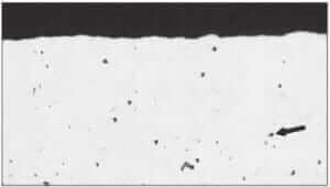 Figure 3.6 Pitting (arrow) on the surface of a cold-drawn brass (Cu-20% Zn) specimen (100X).